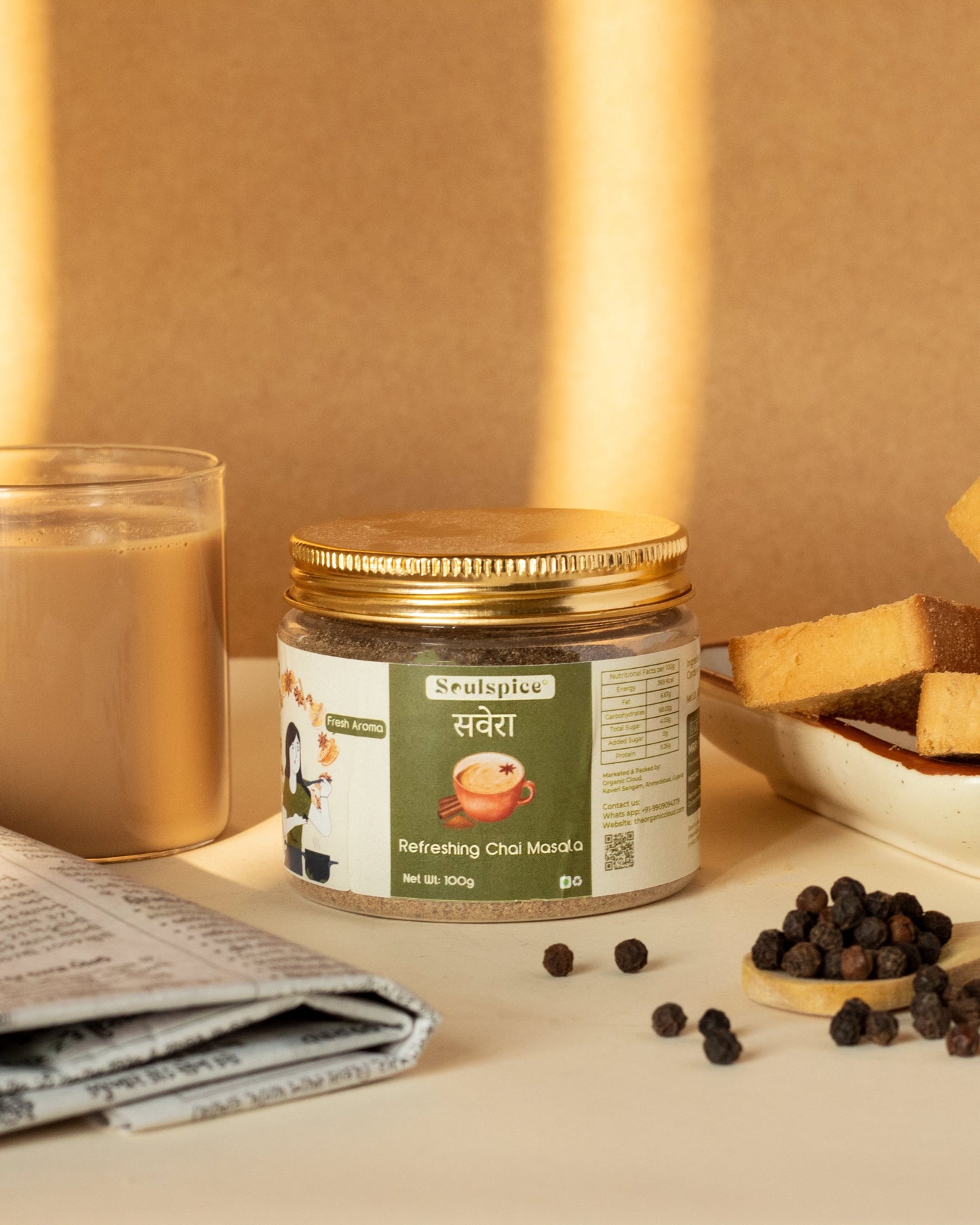 Jar of tea, newspaper, cup of tea, and snacks on a table with a warm background